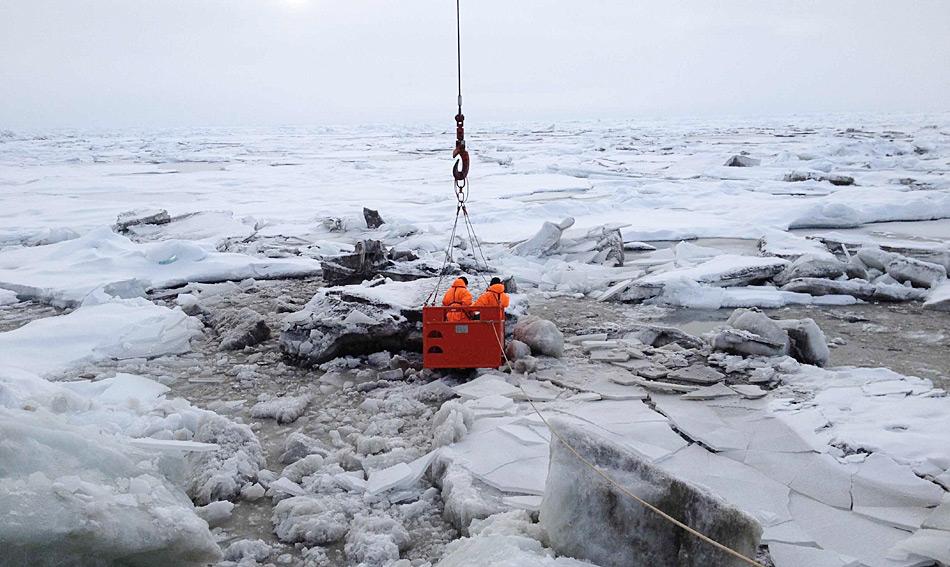 Teilnehmer der Polarstern-Expedition nehmen am 31. August 2014 in der zentralen Arktis Meereisproben. Aus Sicherheitsgründen stehen sie dazu im sogenannten Mummy Chair, der vom Bordkran auf das Eis gehoben wird. Foto: Ruediger Stein, AWI